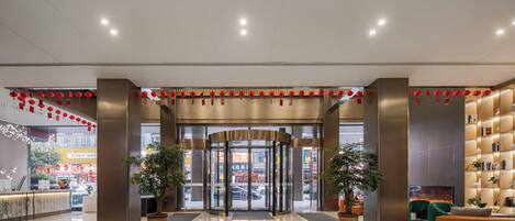 Un moderno vestíbulo de hotel con puerta giratoria, plantas en macetas, mostrador de recepción y zona de estar.