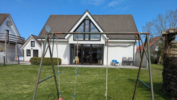 A residential property with a well-maintained lawn, a swing set, and a house with a tiled roof and large windows. - Time out at the North Sea - cozy vacation apartment with garden, 400m from the dike (Wurster Nordseeküste - Dorum - Neufeld)