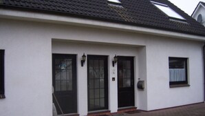 A white building with a tiled roof, three black doors, and a small window with a curtain. - Time out at the North Sea - cozy vacation apartment with garden, 400m from the dike (Wurster Nordseeküste - Dorum - Neufeld)
