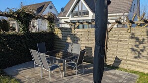 A patio with a table and chairs, a black umbrella, and a stone wall. - Time out at the North Sea - cozy vacation apartment with garden, 400m from the dike (Wurster Nordseeküste - Dorum - Neufeld)