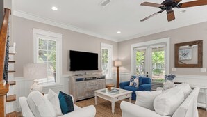 A living room with white furniture, a flat-screen TV, and a ceiling fan.