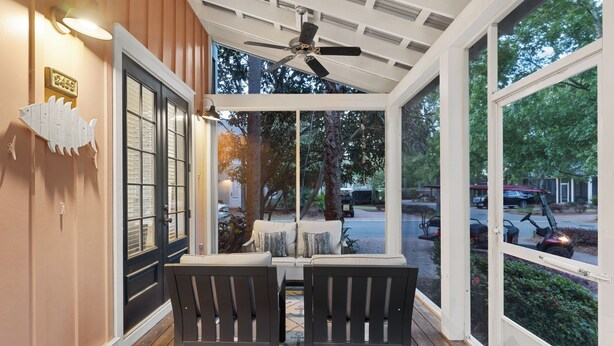 A covered porch with two chairs, a ceiling fan, and a view of the street.