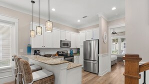 A modern kitchen with white cabinets, stainless steel appliances, a central island with bar stools, and pendant lighting.