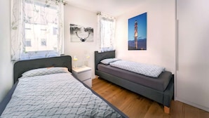 Et soveværelse med to senge, et natbord, en lampe og billedkunst på væggene.