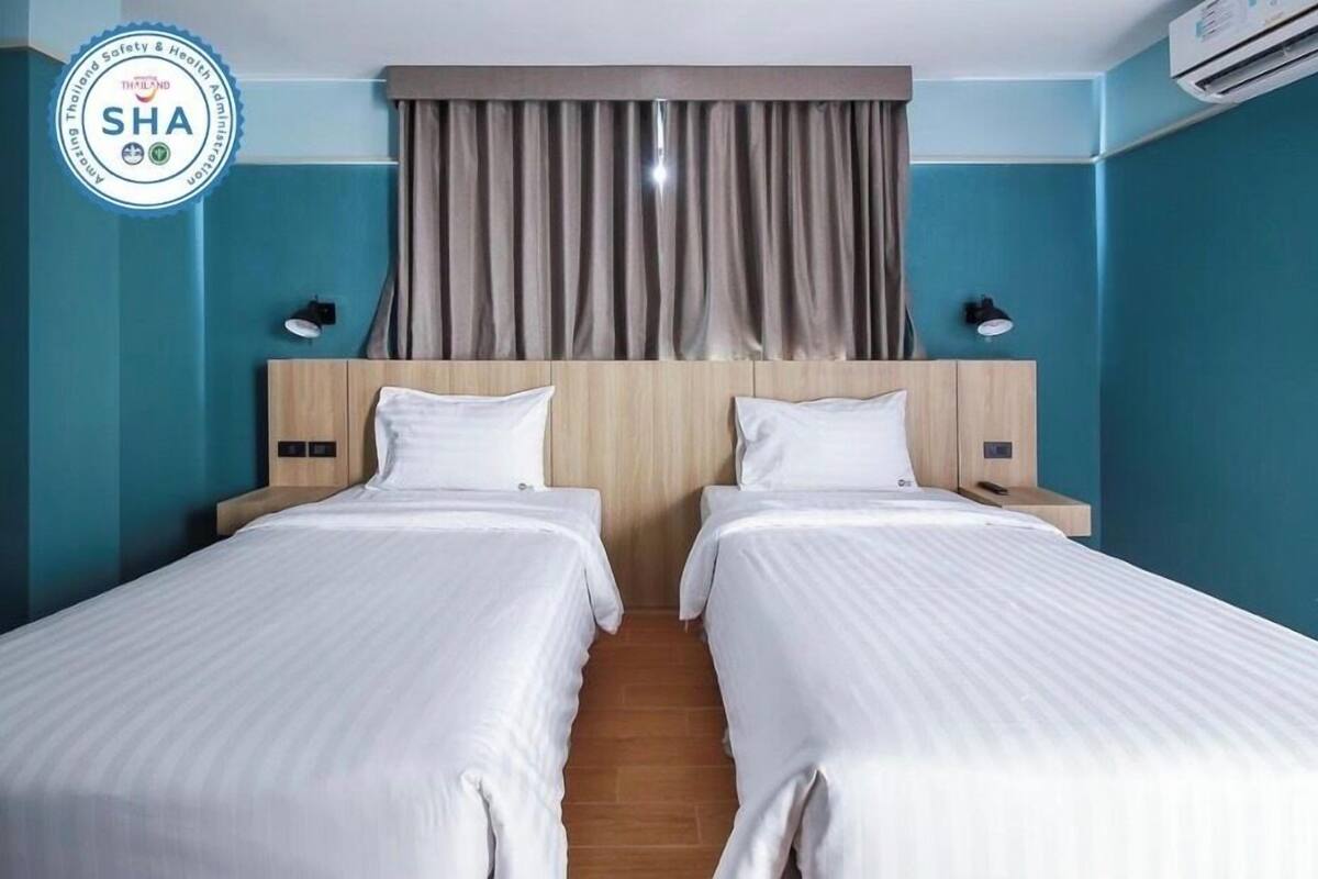 Una camera d'albergo con due letti, pareti color verde acqua, una testiera in legno e una tenda.