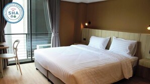 A hotel room with a large bed, a bedside table, a chair, and a window with curtains. - Mybed Chonburi (Chonburi)