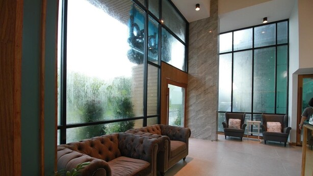 A spacious lobby with a large window, a leather sofa, and a seating area with chairs and a small table. - Mybed Chonburi (Chonburi)
