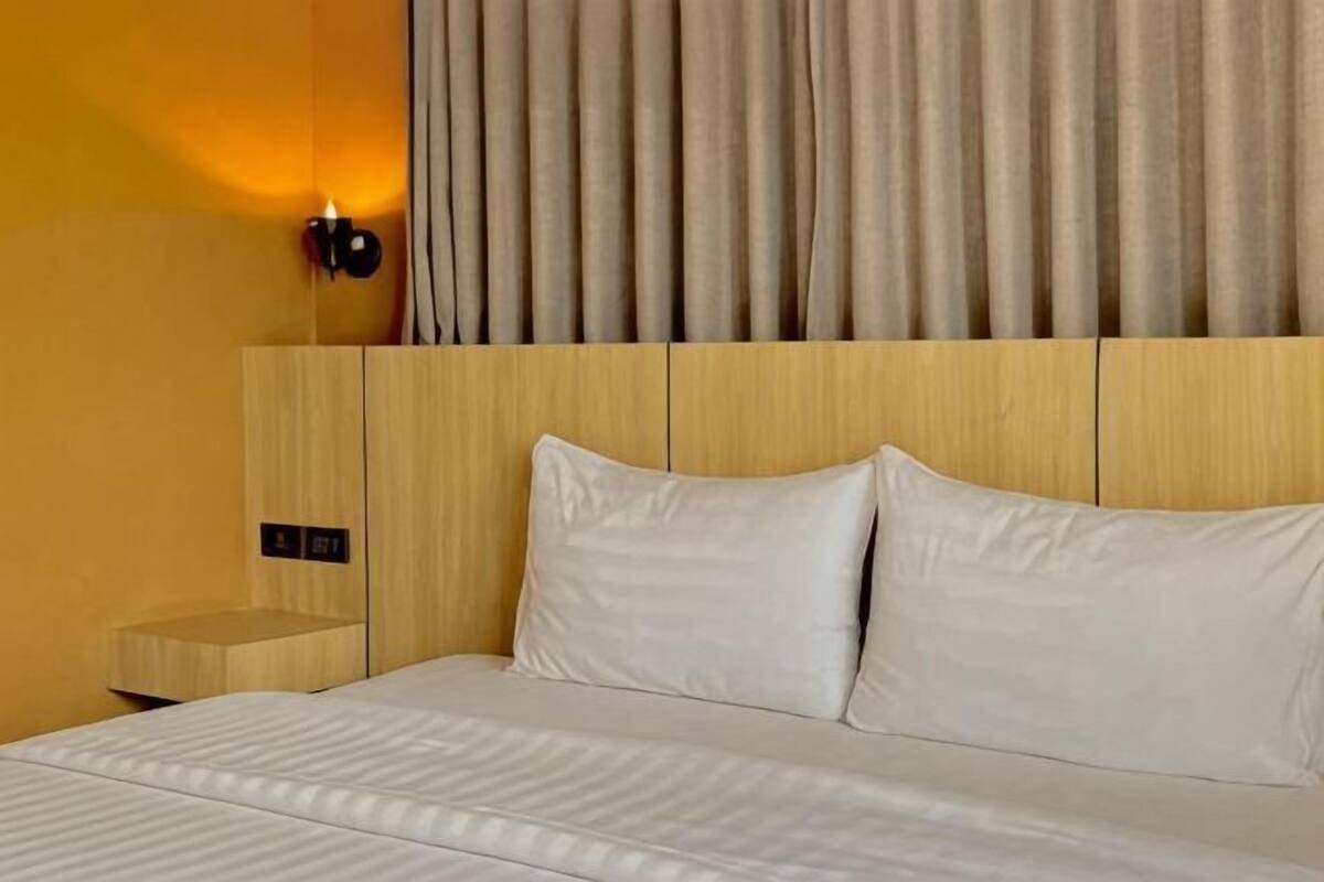 Una camera d'albergo con un letto, un comodino, una lampada a parete e una tenda.