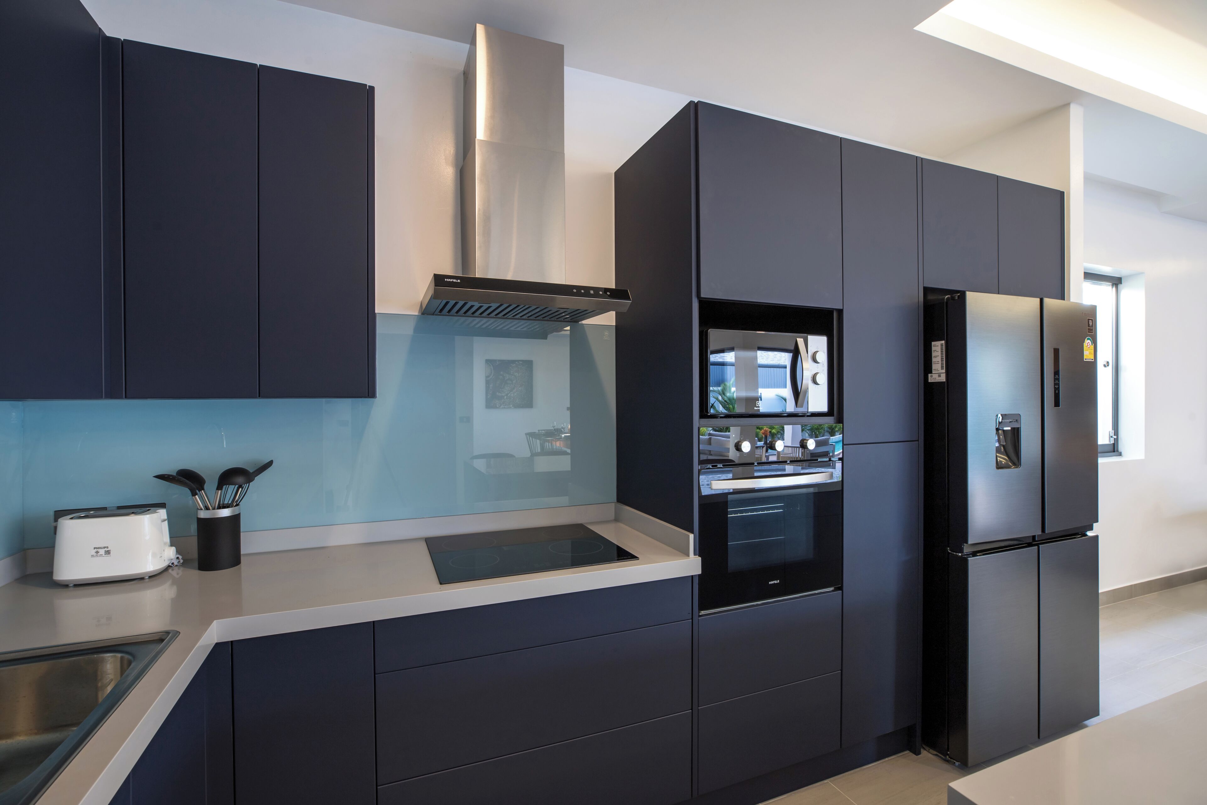 A modern kitchen with dark cabinetry, a built-in oven, a refrigerator, and a toaster on the countertop.