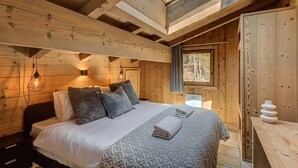 A cozy wooden bedroom with a skylight, a bed with grey bedding, and a small table with towels.