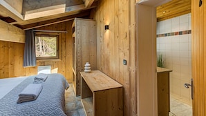 A wooden cabin with a skylight, a bed with towels, a small table, and a bathroom with a tiled shower area.