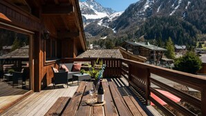 A wooden deck with outdoor seating, overlooking a mountainous landscape with snow-capped peaks.