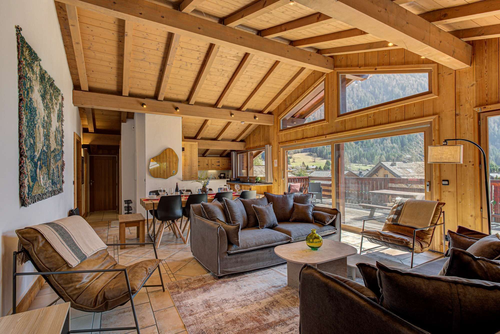 A spacious living area with a high ceiling, wooden beams, large windows, and a view of the outdoors.