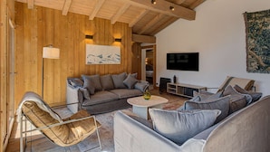 A cozy living room with a wooden ceiling, a large sofa, a coffee table, and a TV.