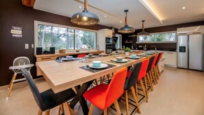 A modern kitchen with a dining area, large windows, and a view of the outdoors.