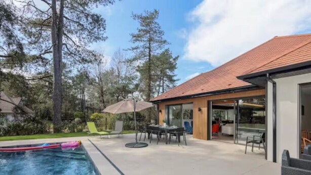 A modern outdoor pool area with a patio, seating, and a building with large windows.