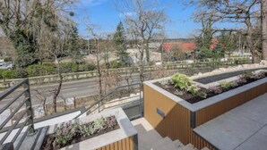 A modern outdoor area with a wooden bench, a metal railing, and a view of a road and trees.