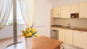 A modern kitchen with a stove, sink, and cabinets. There is a window with curtains and a vase of yellow flowers on the table. - Classic Appartement in Pietra Ligure (Pietra Ligure)