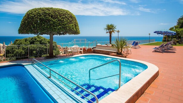 A swimming pool with a clear view of the ocean, surrounded by lounge chairs and a palm tree. - Classic Appartement in Pietra Ligure (Pietra Ligure)