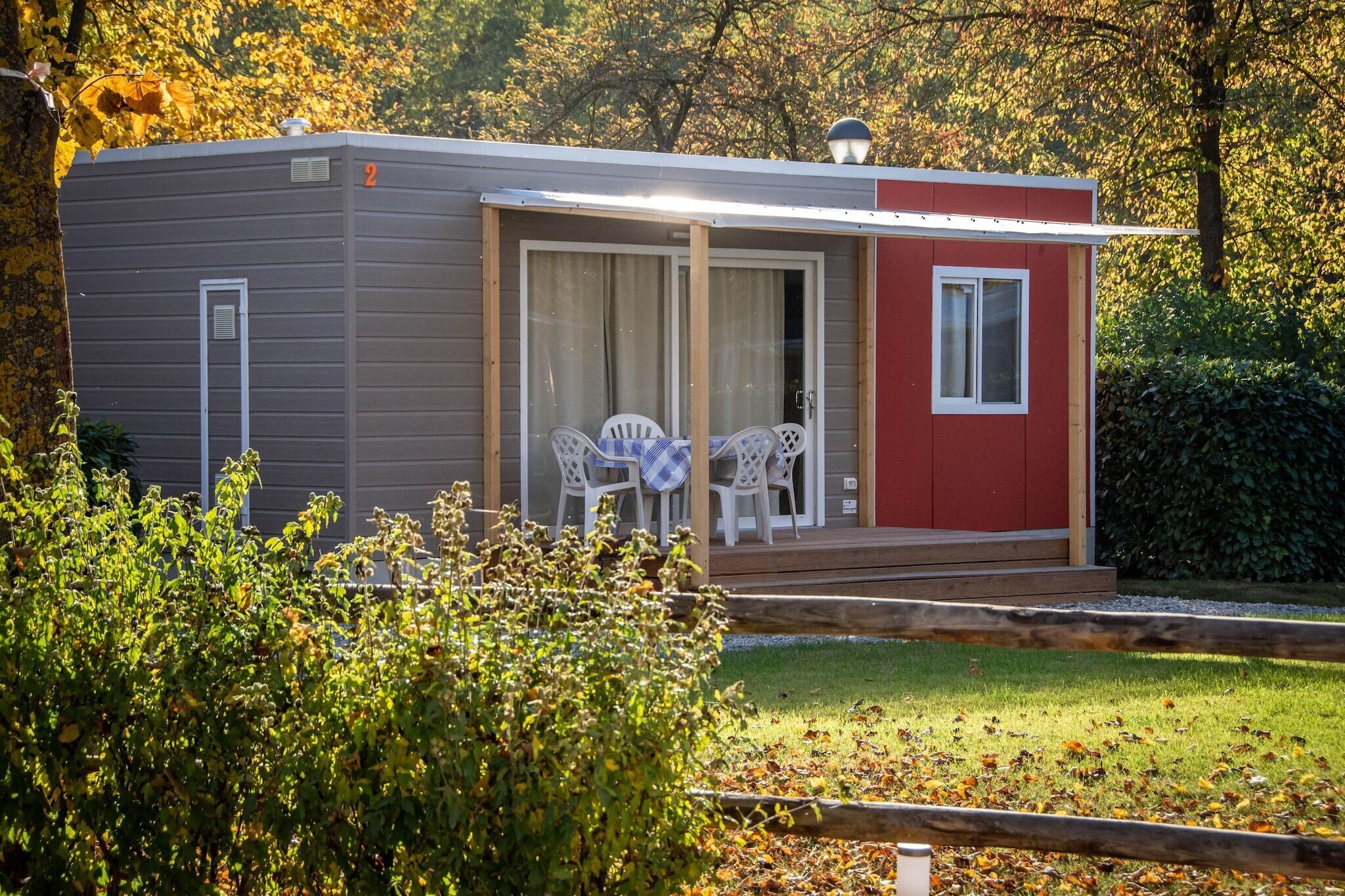 A small, single-story cabin with a sliding glass door, a small porch with a table and chairs, and a red exterior wall.