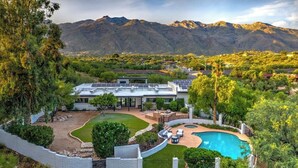 A modern house with a swimming pool, surrounded by a landscaped garden and a view of mountains.