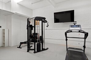 Une salle de sport équipée d’une machine de musculation, d’un banc et d’un tapis de course.