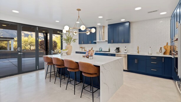 A modern kitchen with a central island, bar stools, and blue cabinets.