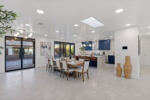 A modern kitchen with dark blue cabinets, a central island, and a dining area with a large table and chairs. - Designer Luxury  Home w/Pool & Hot Tub Foothills (Tucson)
