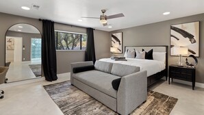 A modern bedroom with a large bed, a sofa, a nightstand, and a ceiling fan.