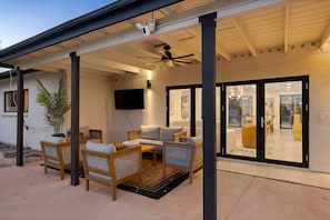A covered outdoor seating area with wicker furniture, a ceiling fan, and a television mounted on the wall.