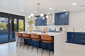 A modern kitchen with a central island, bar stools, and a large window overlooking a mountainous landscape.