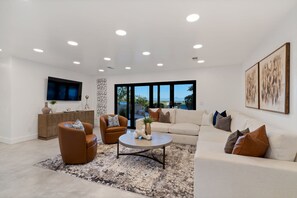 A modern living room with a sofa, armchairs, a coffee table, and a TV.