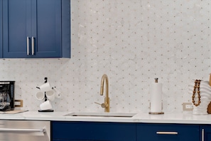 Eine Küche mit blauen Schränken, einer weißen Arbeitsplatte, einem goldenen Wasserhahn und einer Kaffeemaschine.