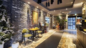A modern interior with a brick wall, a dining area with yellow chairs, and a kitchen area. - AVENUE HOTEL (Osan)