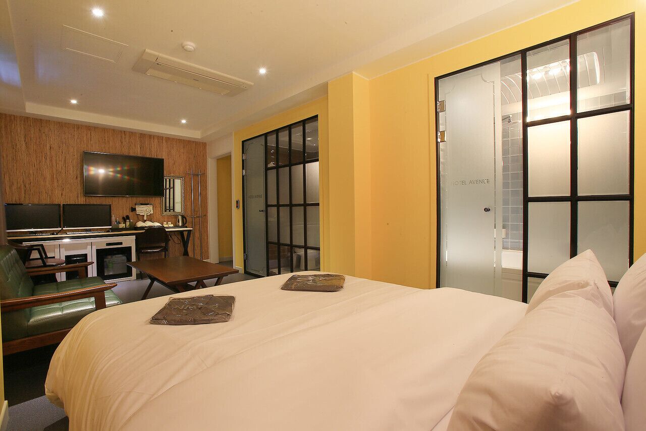 Une chambre d’hôtel comprenant un lit, un bureau avec une chaise, une télévision et une salle de bain dont les portes sont en verre dépoli.