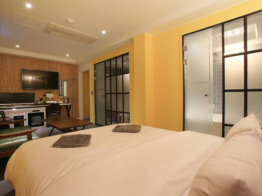 Une chambre d’hôtel comprenant un lit, un bureau avec une chaise, une télévision et une salle de bain dont les portes sont en verre dépoli.