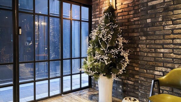 A room with a large window, a brick wall, and a potted plant. - AVENUE HOTEL (Osan)