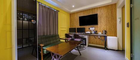 Habitación de hotel pequeña con kitchenette, un sofá verde, una mesa de comedor de madera y un televisor montado en la pared.