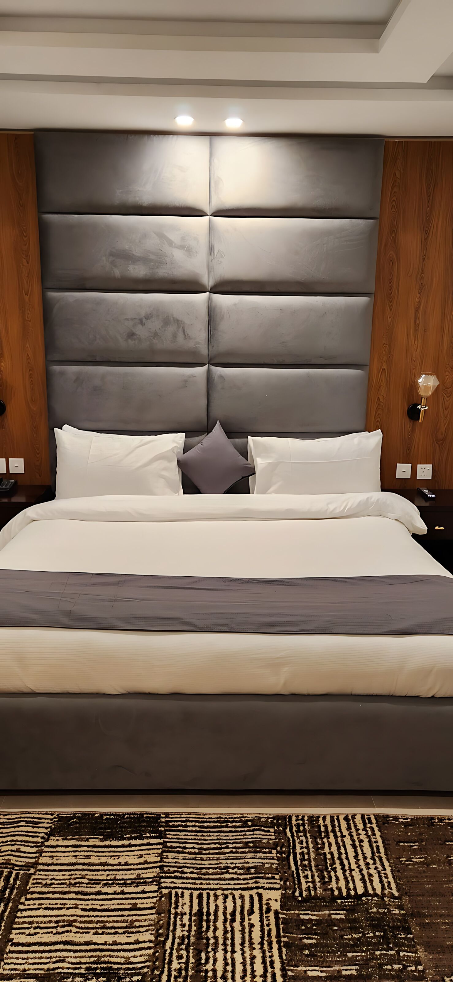 A modern bedroom with a large bed, padded headboard, and a patterned rug.