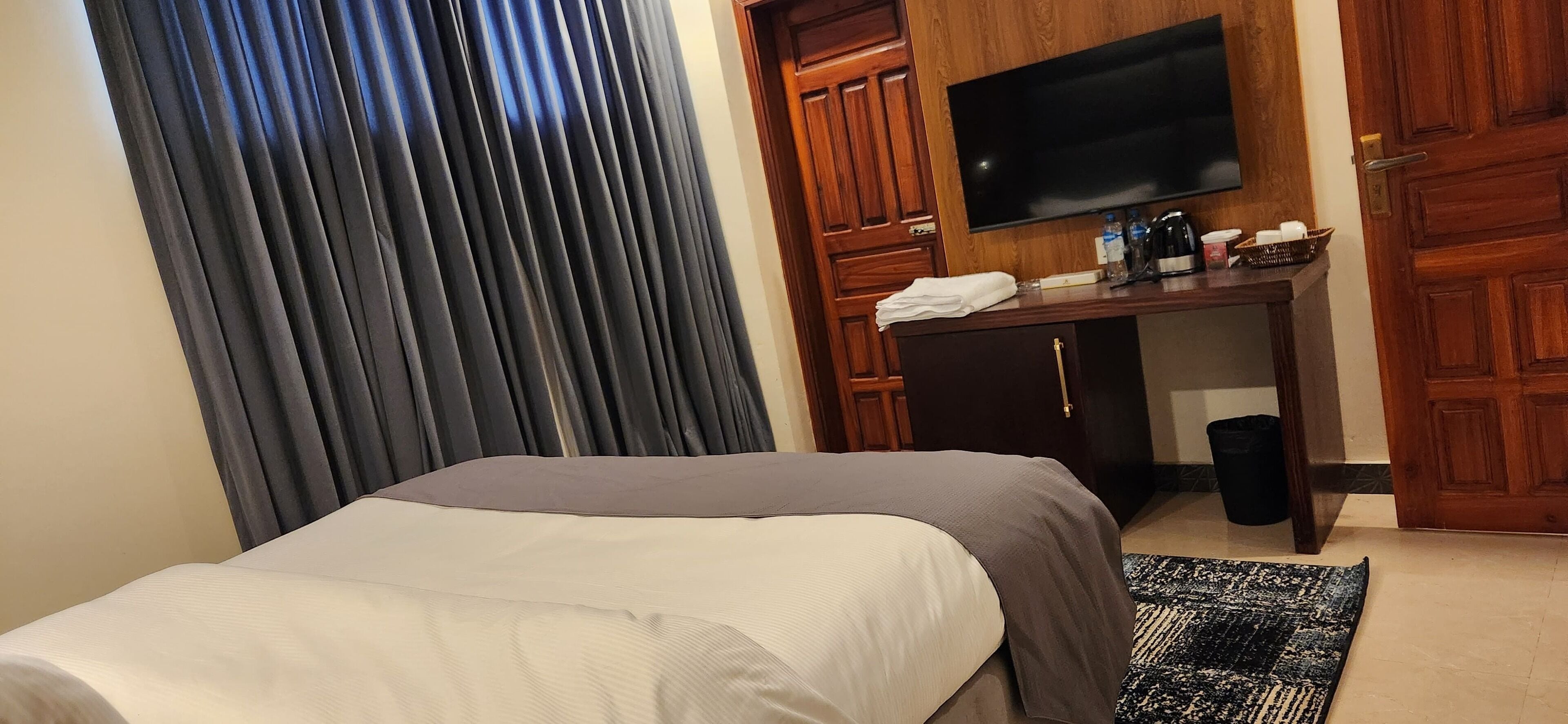 Une chambre d’hôtel comprenant un lit, un bureau avec un téléviseur à écran plat, une armoire en bois et une fenêtre avec des rideaux.