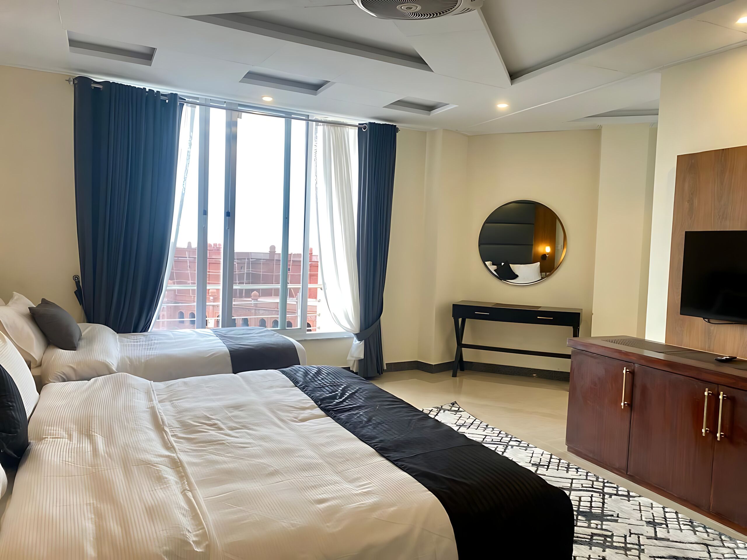 Une chambre d’hôtel avec deux lits, un bureau, une télévision et une grande fenêtre avec des rideaux.