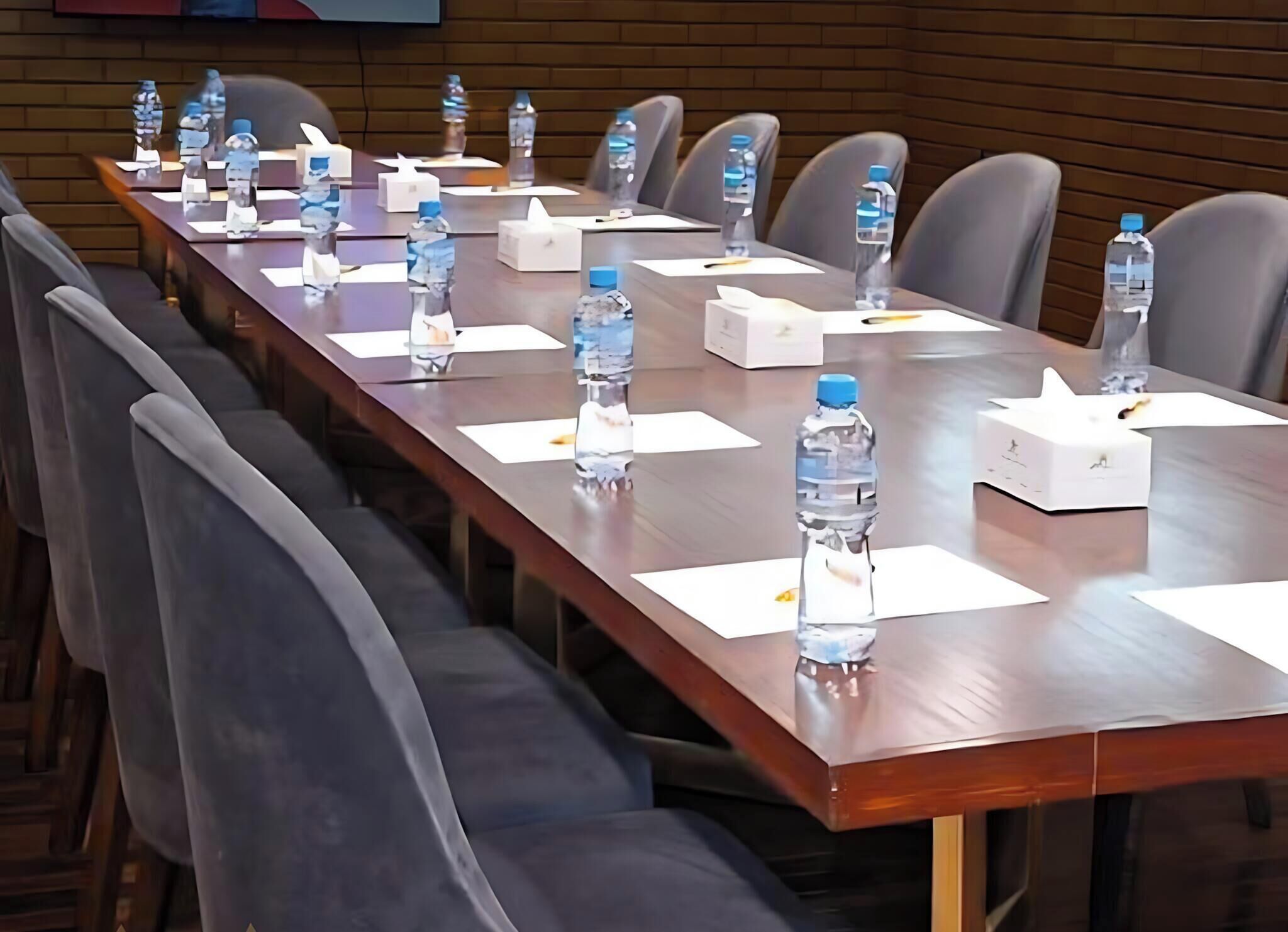 A conference room with a long table, chairs, water bottles, and tissues.