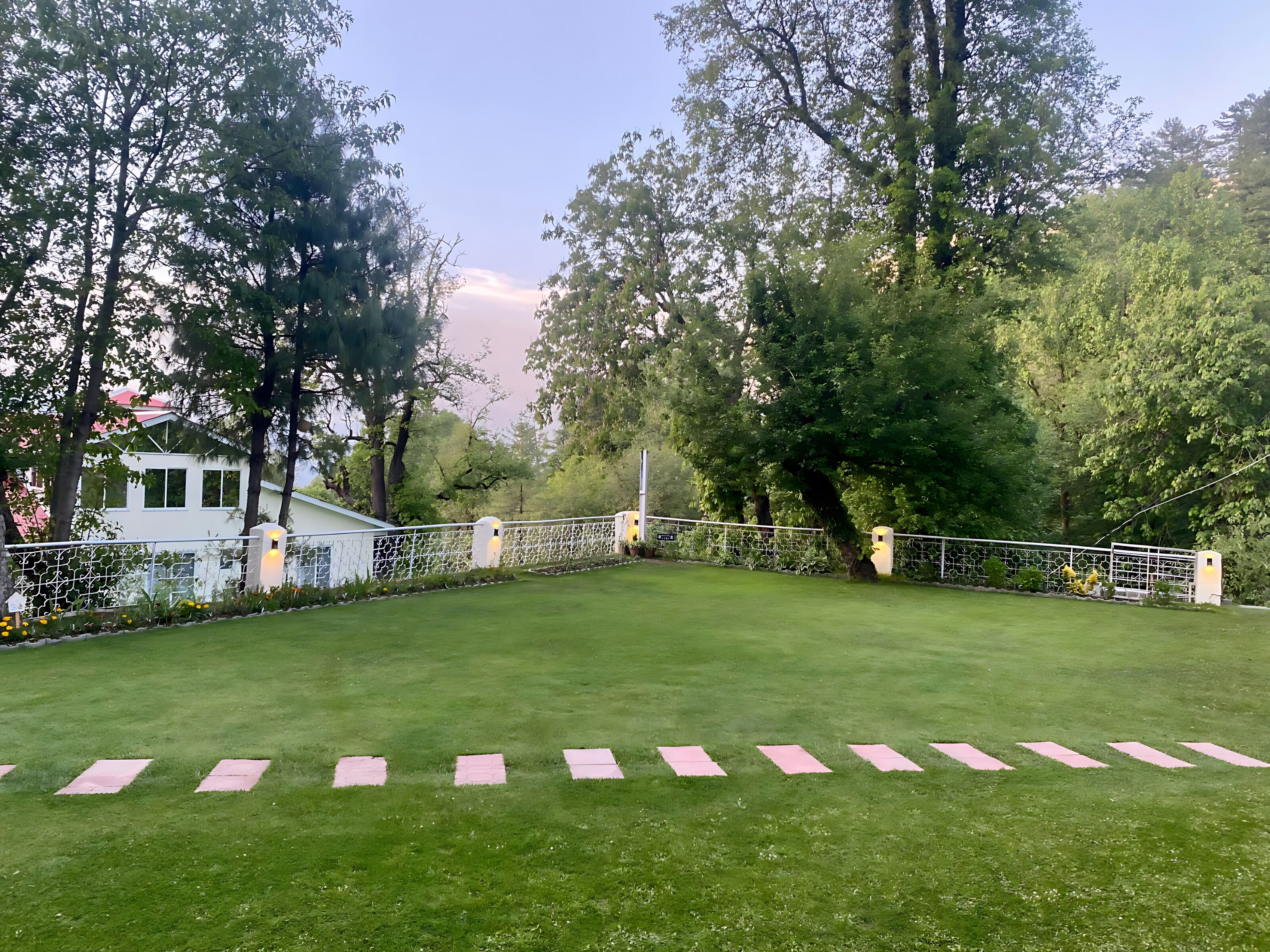 Jardim bem cuidado com cerca branca e caminho demarcado por azulejos cor-de-rosa.