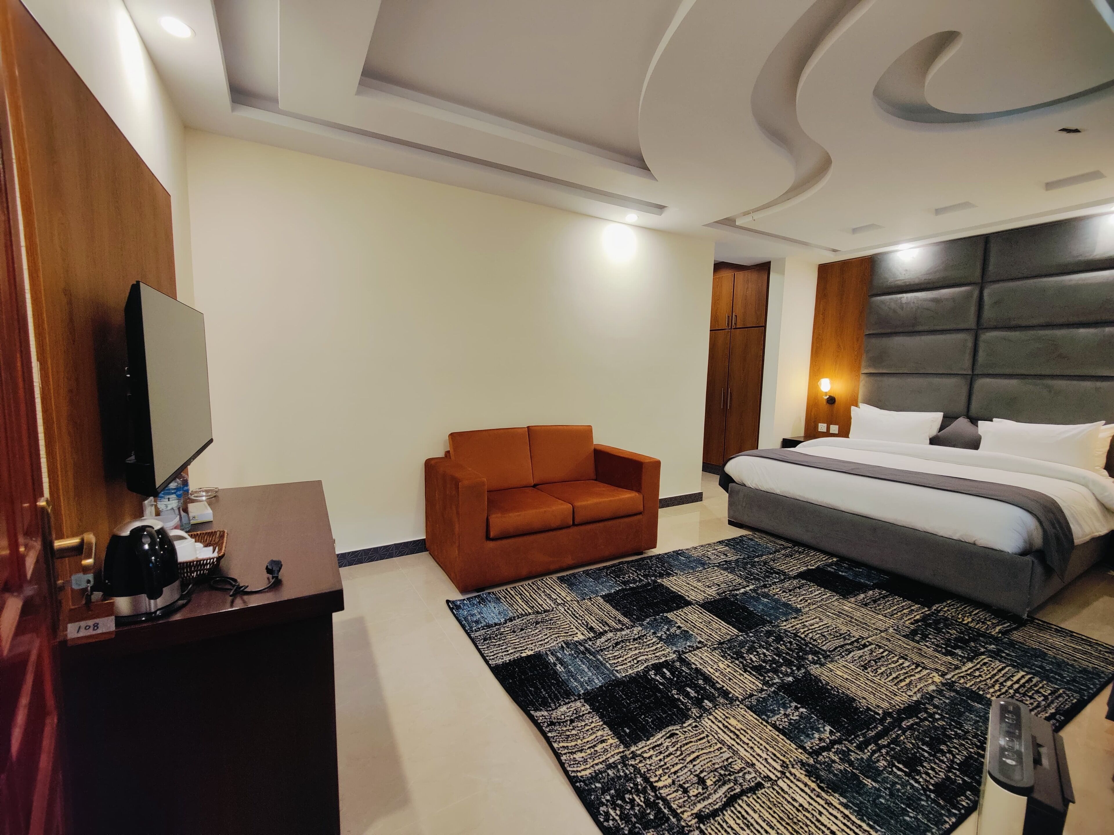 Una habitación de hotel moderna con una cama, un sofá, un escritorio con una computadora y una televisión.