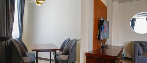 A hotel room with a dining area, a TV mounted on the wall, and a round mirror.