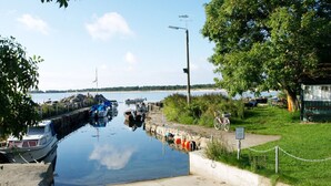 Un rivage paisible où sont amarrés des bateaux, un ciel dégagé et une zone herbeuse avec un banc.