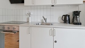 Une cuisine avec des meubles blancs, un évier en acier inoxydable, une machine à café et une cuisinière.