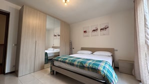 A bedroom with a bed, a wardrobe, a mirror, a bedside table, and three wall art pieces.