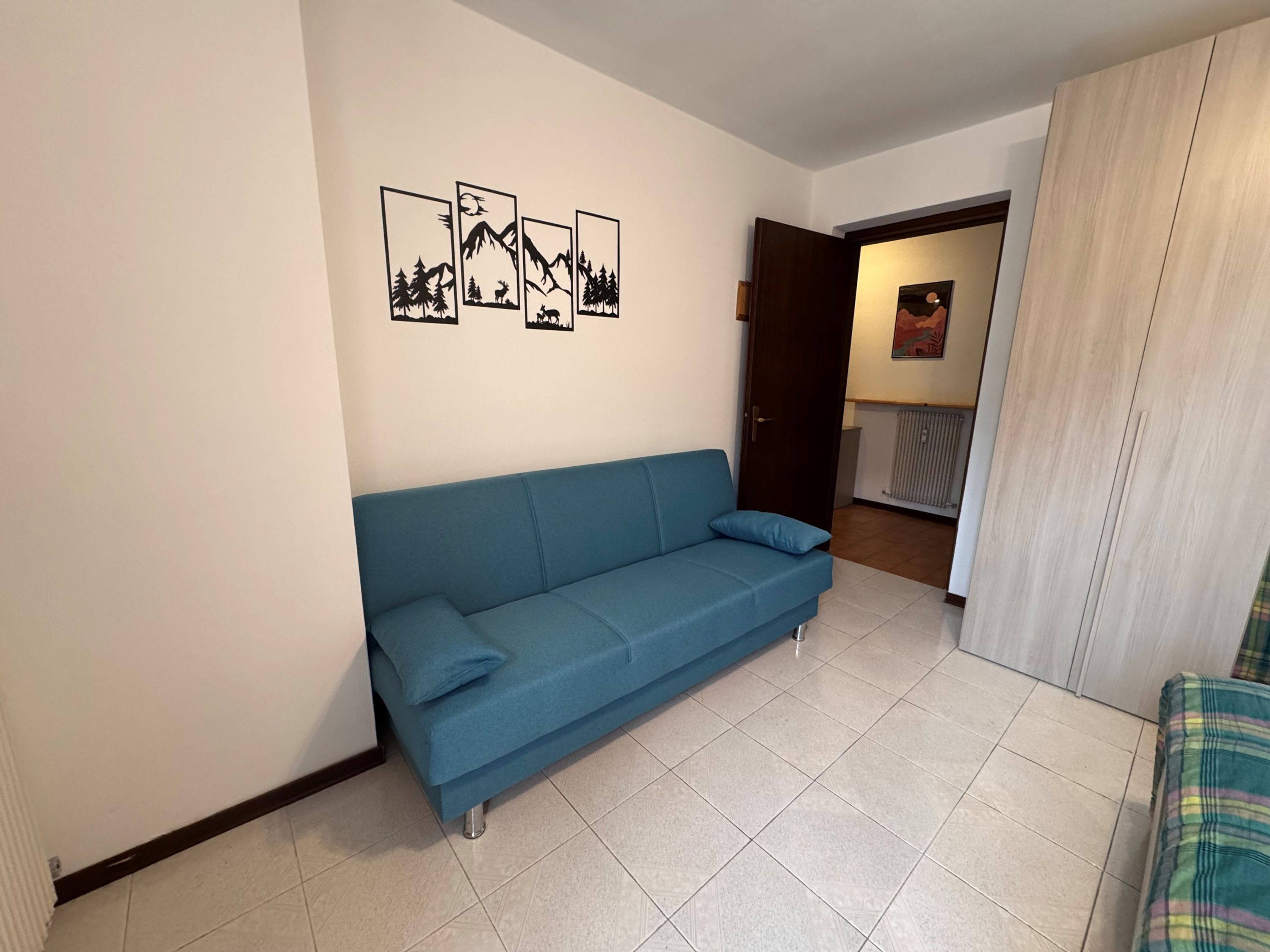 Una sala de estar con un sofá azul, un cuadro colgado en la pared y una puerta que da a otra habitación.