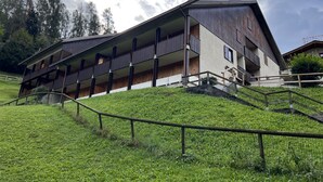 A multi-story building with balconies, a staircase, and a grassy slope.